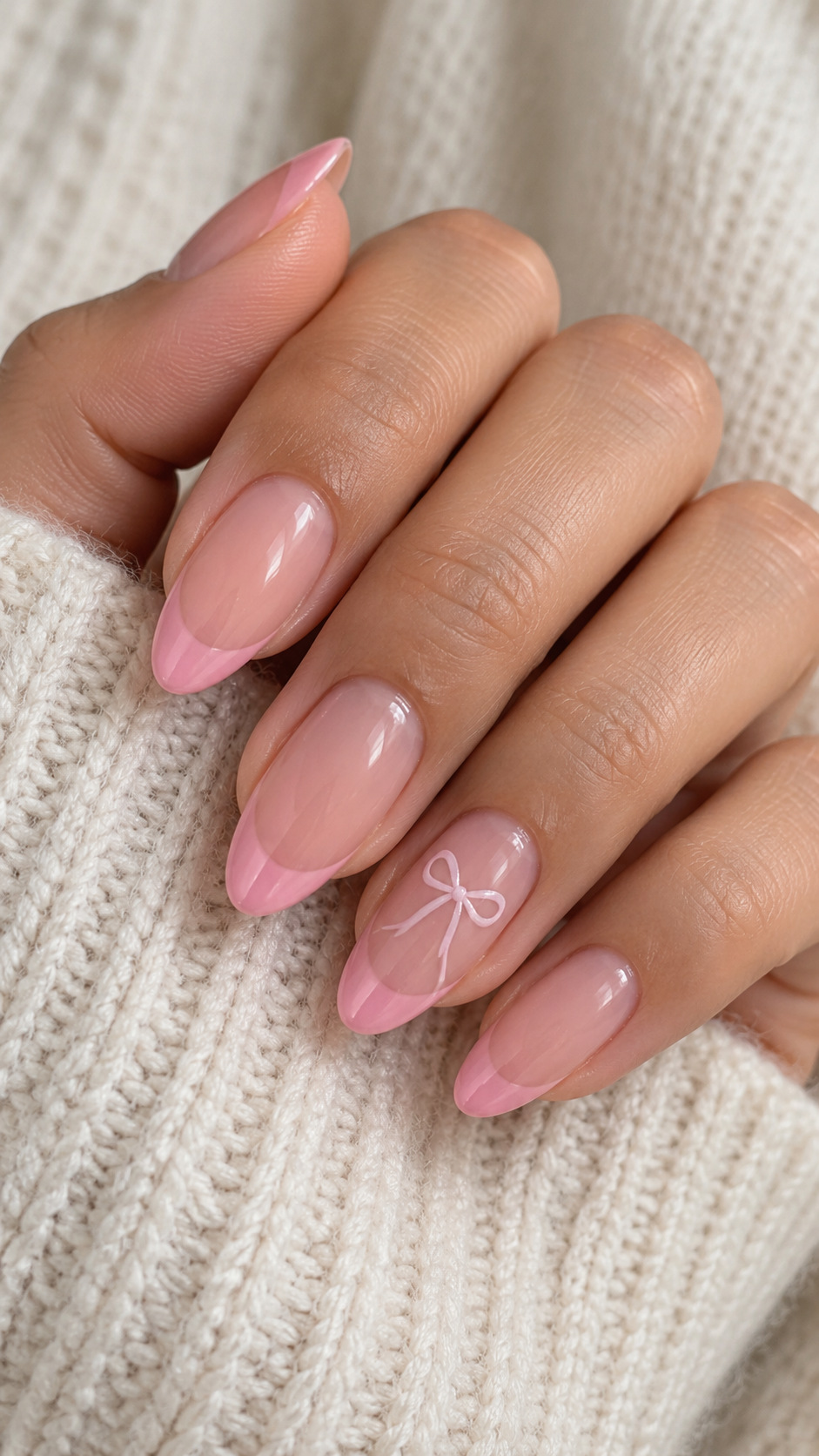 Pink French with a Painted Bow: Pink French almond nails with a fine pale bow below one tip on a naturally posed adult hand