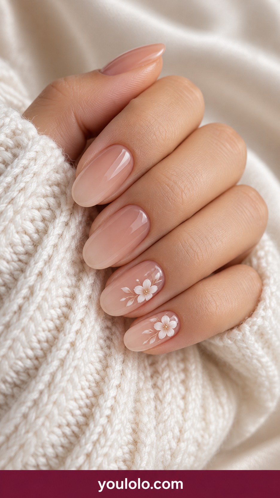 Medium oval translucent beige nails with delicate white five petal blossoms painted at one corner of two nails on a naturally curled young adult hand
