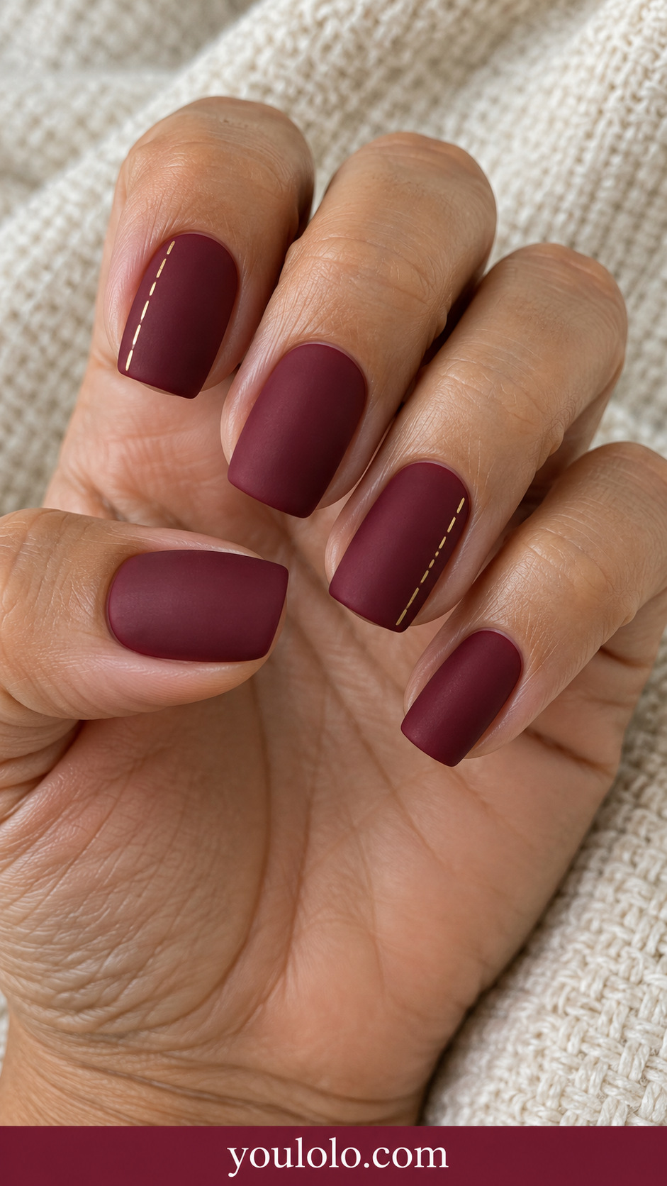 medium squoval matte wine red nails with ONLY a fine straight gold dashed stitch line along one lateral edge on two accent nails, no other motifs, no leaves, no vines, no flowers, no botanicals on a naturally relaxed adult hand