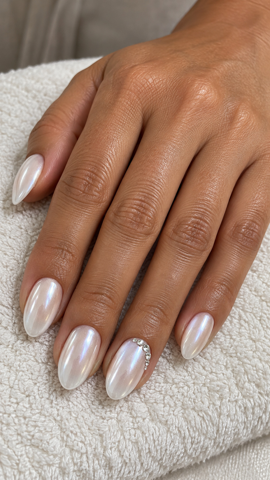 White Chrome with a Crystal Crescent: Pearly white oval nails with a small rhinestone crescent on the ring finger on a naturally posed adult hand