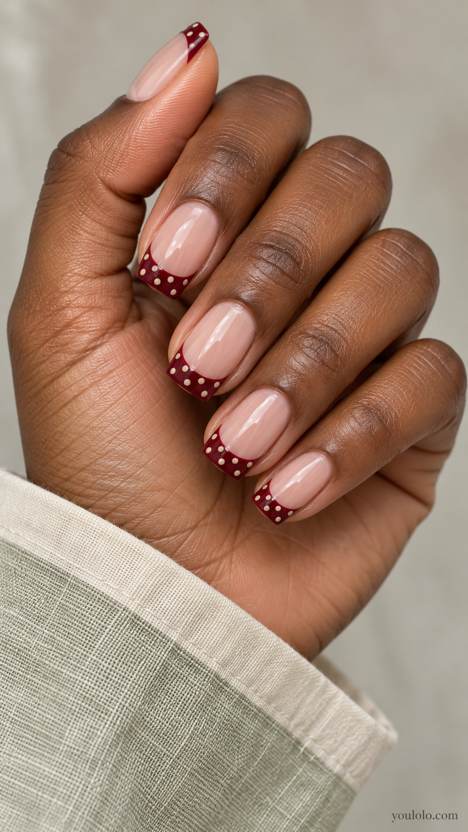 Medium soft square nails, nude base, burgundy French tip bands containing tiny cream polka dots, nude nail beds empty.