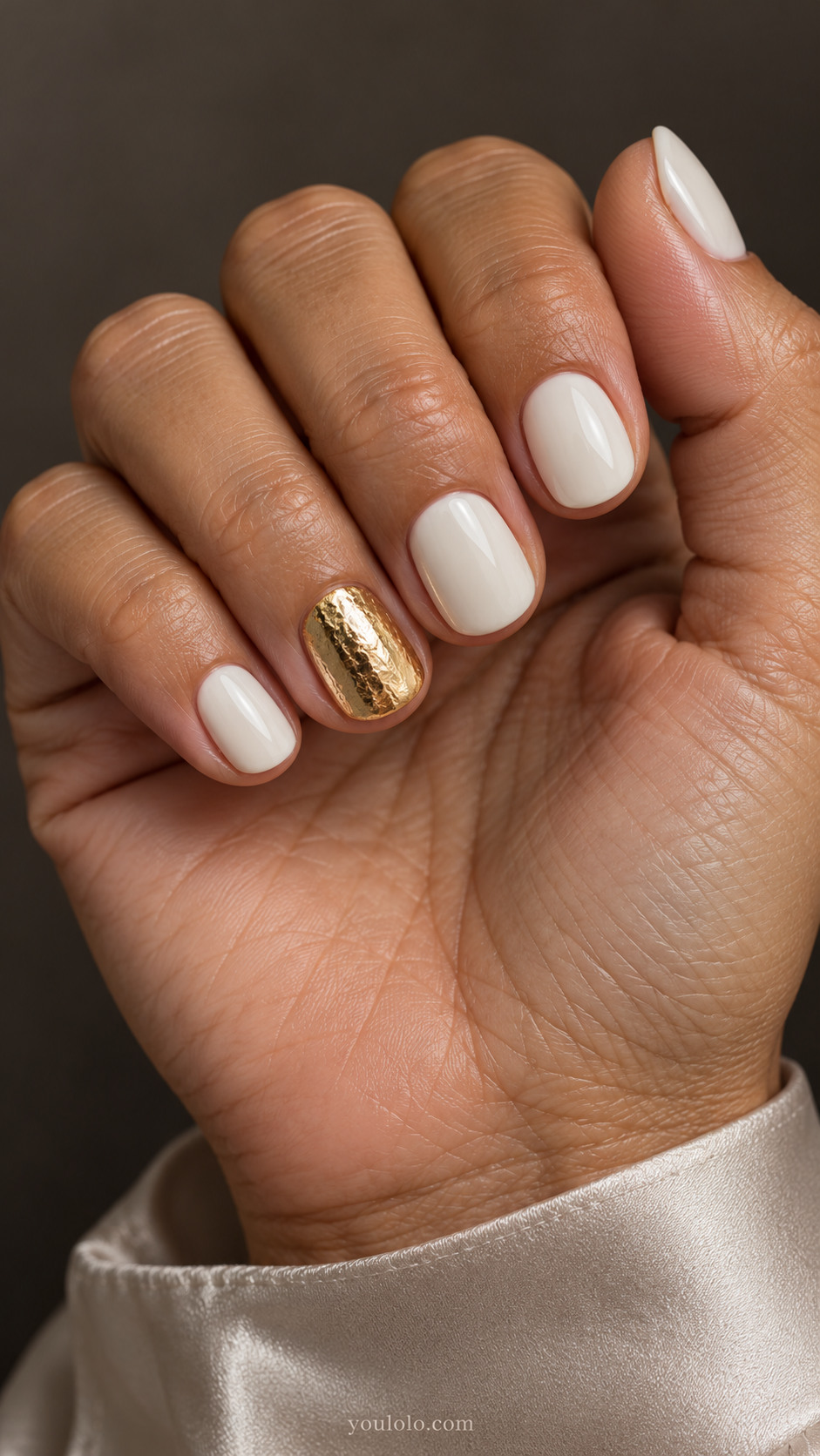 Short rounded ivory nails with one fully gold ring nail in a smooth hammered-foil effect