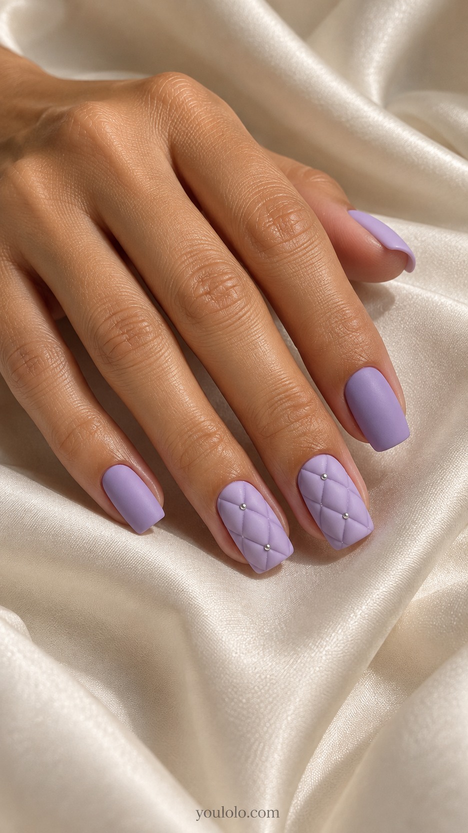 Lavender Quilted Nails — Medium square nails, lavender matte base, two accent nails with low raised softly padded diamond quilt panels separated by recessed thin grooves, tiny silver dots only at three intersections, remaining nails smooth lavender