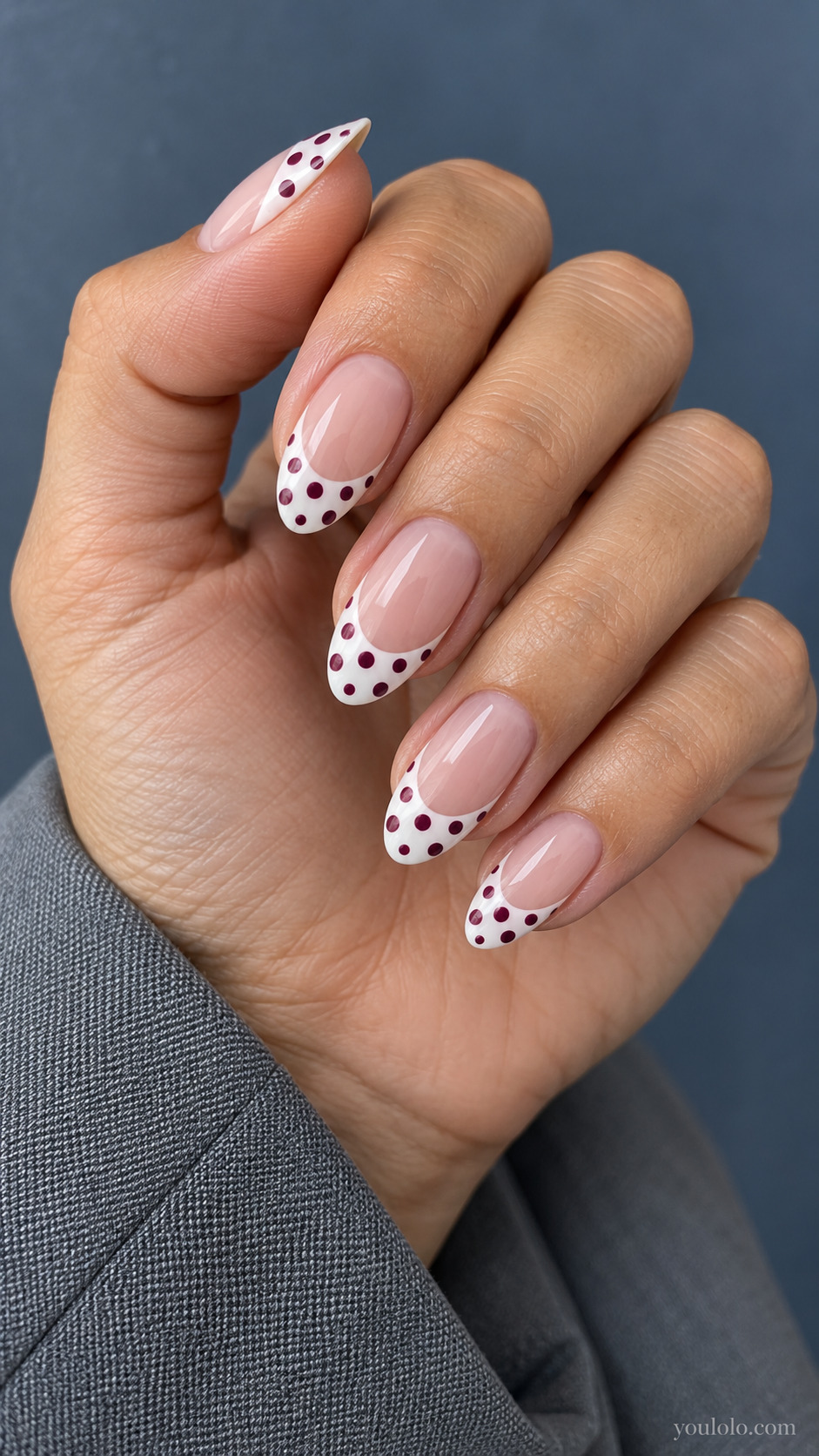 Medium almond nails, sheer nude base and broad curved cream tips decorated with burgundy dots only inside white tips.