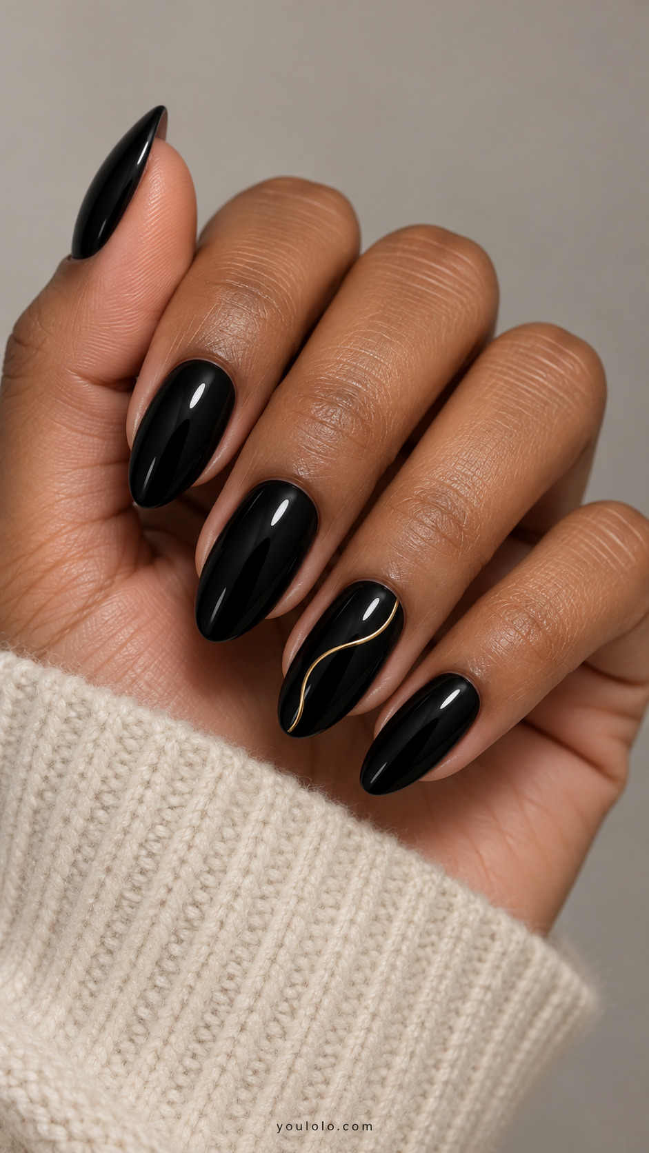 Glossy black almond nails with a fine gold curve on the ring nail