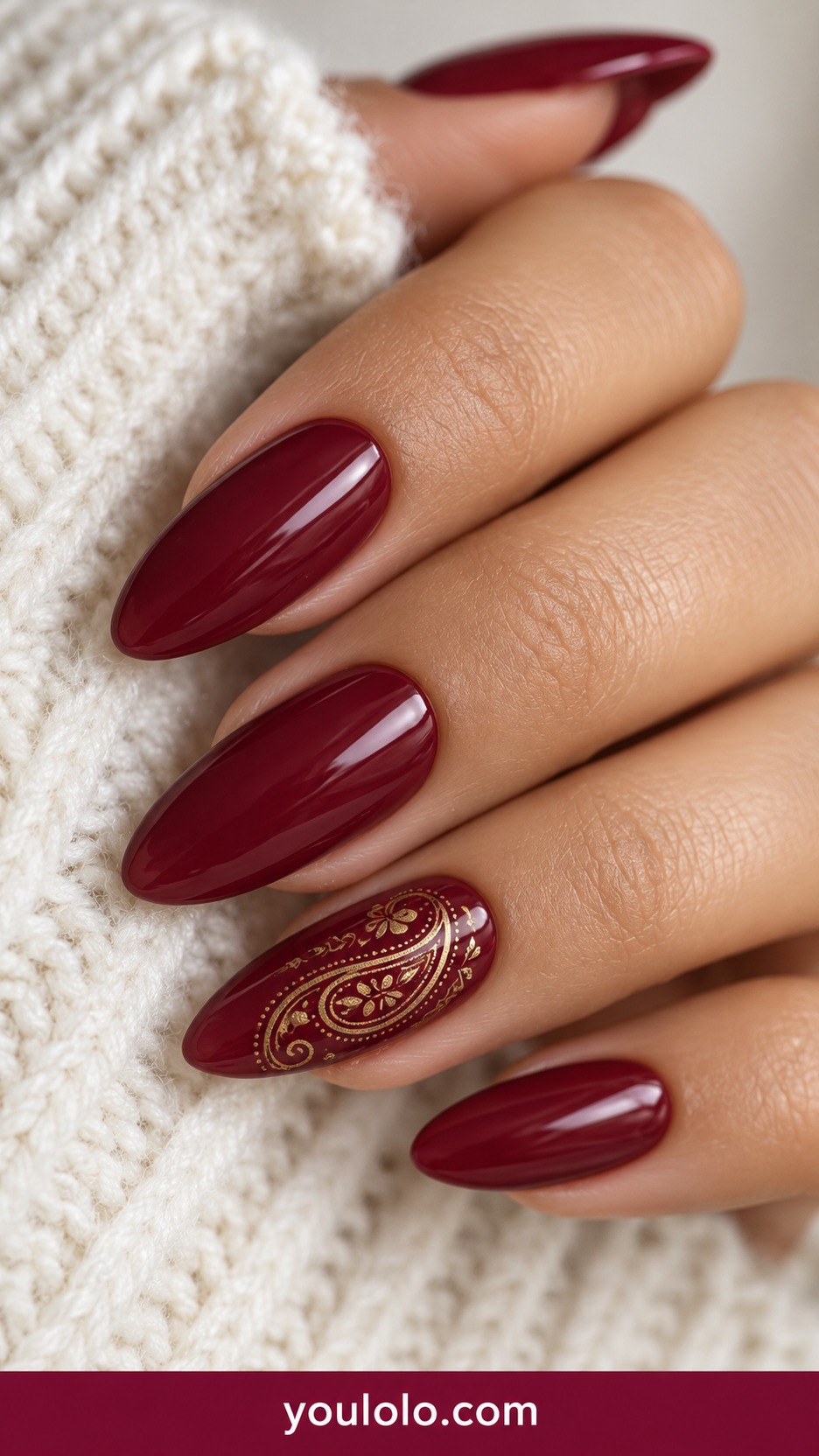 Medium almond burgundy nails with fine muted gold paisley outline on one accent on a naturally curled young adult hand