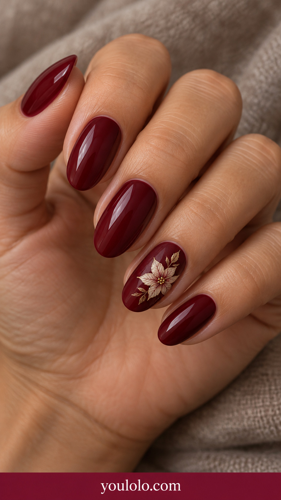 medium oval glossy deep red nails with small fine ivory outlined poinsettia petals and subtle gold center on ring nail only on a naturally relaxed adult hand
