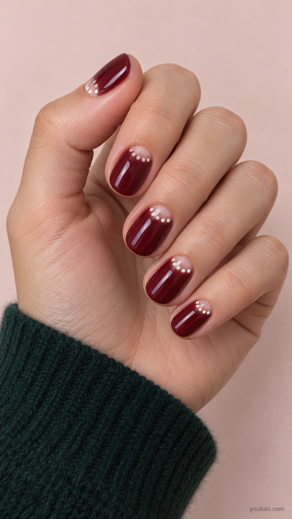 Short round full burgundy nails, small nude half moon at cuticle bordered by neat ivory dots tracing semicircle, remaining wine surface plain.