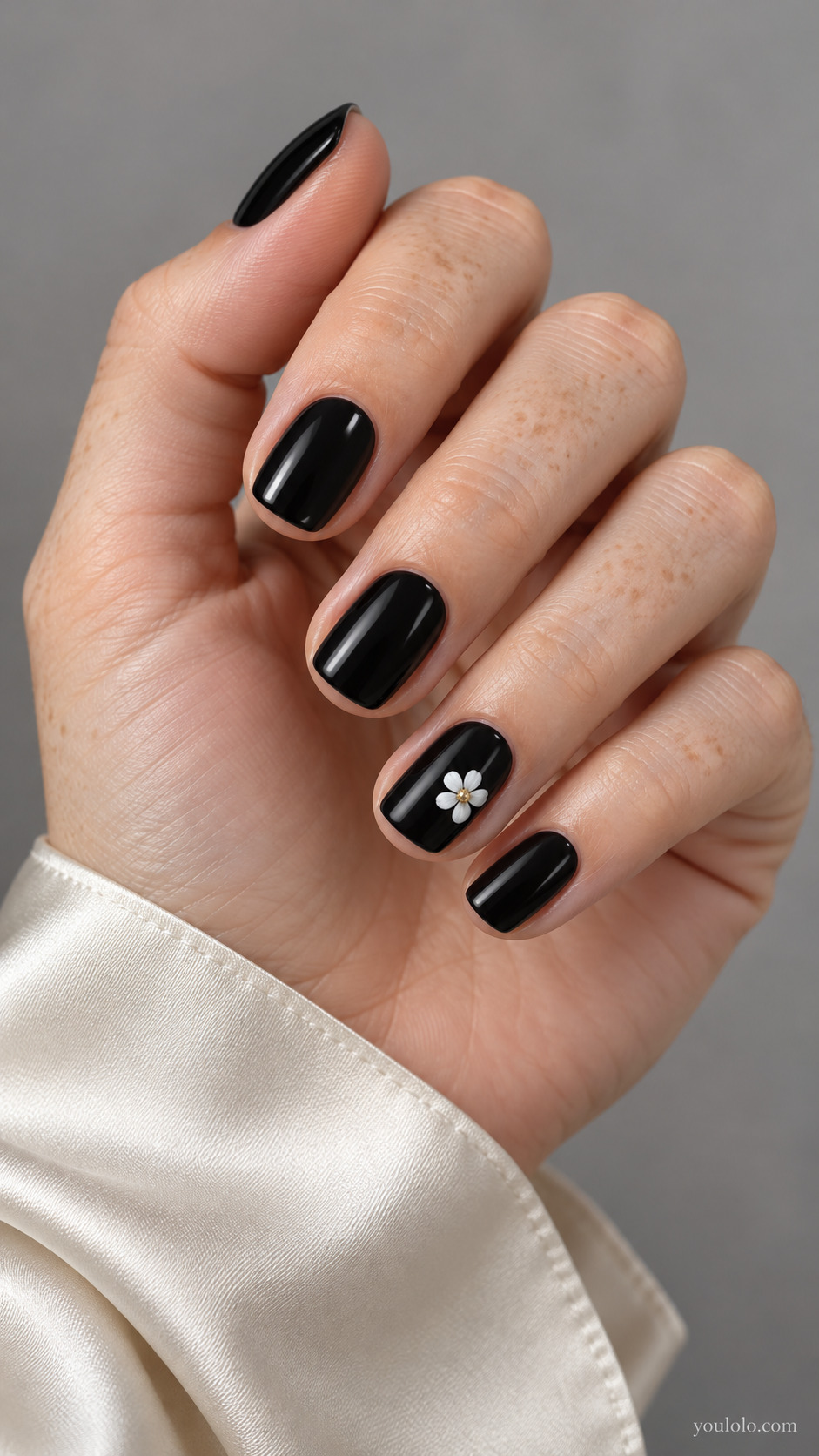 Short glossy black nails with one small white flower accent