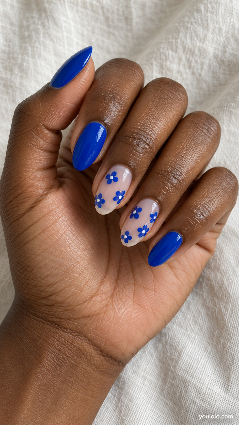 Milky nude almond accent nails with royal blue flowers beside solid blue nails
