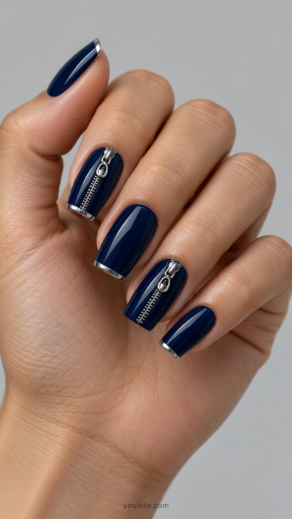 Silver Zipper Nail Art — Medium tapered square nails, opaque ink navy, index and ring nails have miniature silver chrome zipper illusion in low sculpted relief: two tidy rows of small metal teeth with tiny rounded oval zipper pull contained entirely within nail