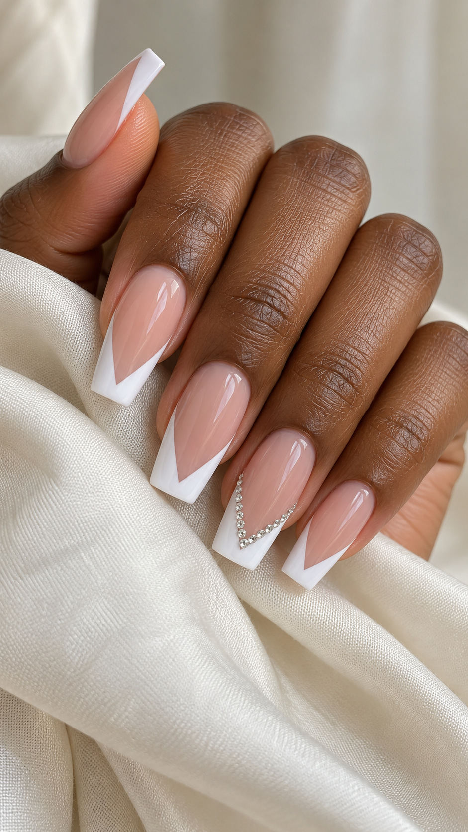 White V-French with a Crystal Border: Long square French nails with a white V tip and a crystal border on one finger on a naturally posed adult hand