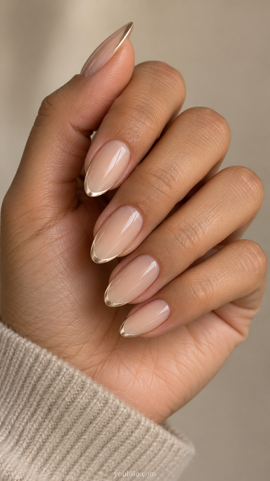 Medium almond nails with a sheer beige base and slender champagne metallic French tips.