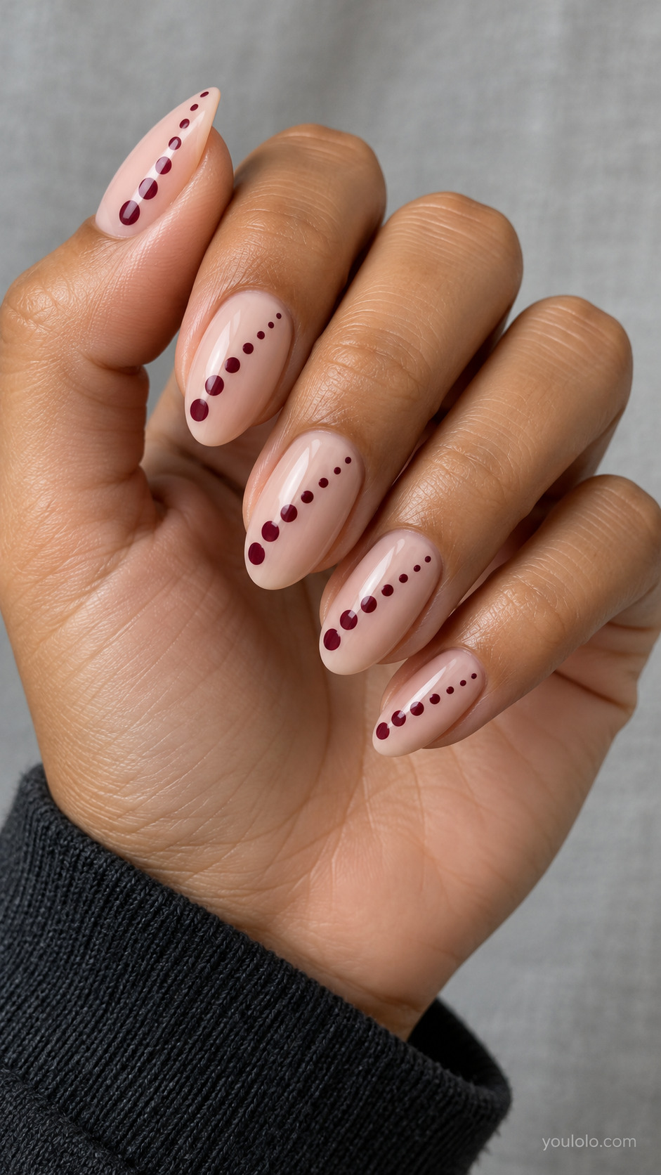Medium almond nude nails, single diagonal trail of burgundy round dots across each nail, progressively smaller toward tip, no connecting line.