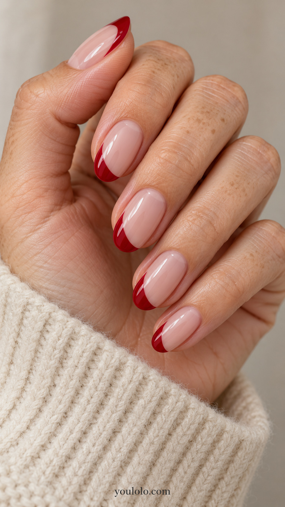 medium oval nude nails, asymmetric cherry red French tip sweeps down one side and fine at opposite side on a naturally gathered hand