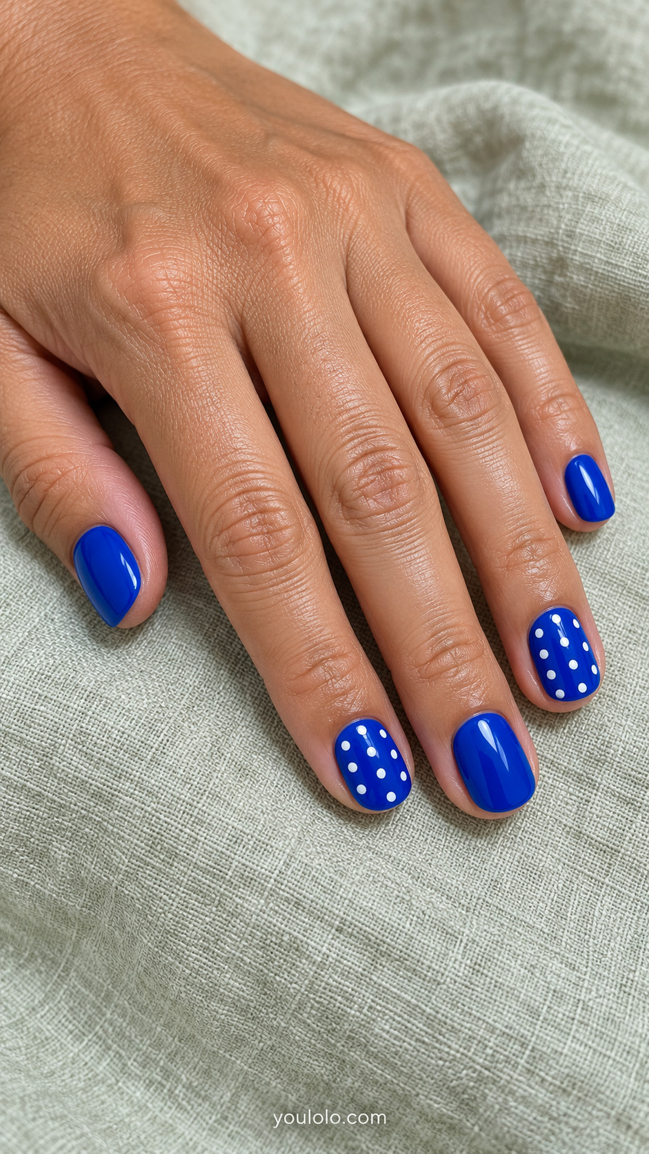 Short royal blue soft-square nails with white polka dots on two accent nails