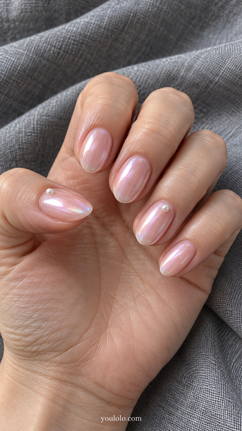Short almond nails sheer pink pearl glaze, one tiny low profile ivory flat backed pearl at center near cuticle of ring nail and thumb only, other nails plain