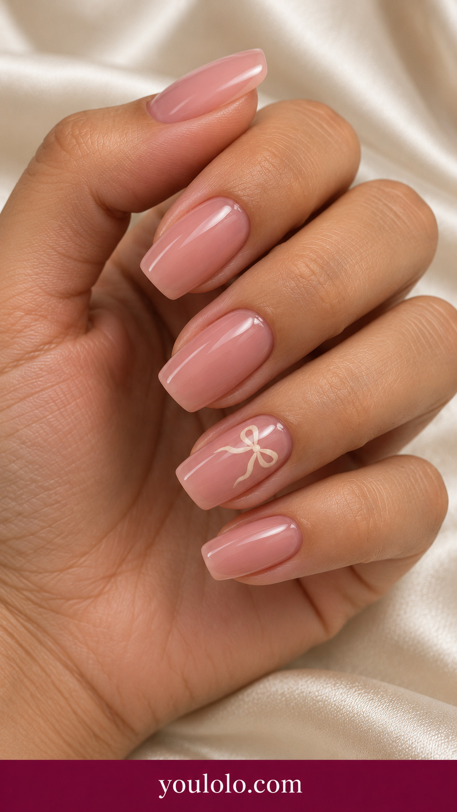 medium soft square dusty pink press-on nails with one tiny flat painted ivory bow on ring nail, others plain dusty pink on a naturally posed adult female hand