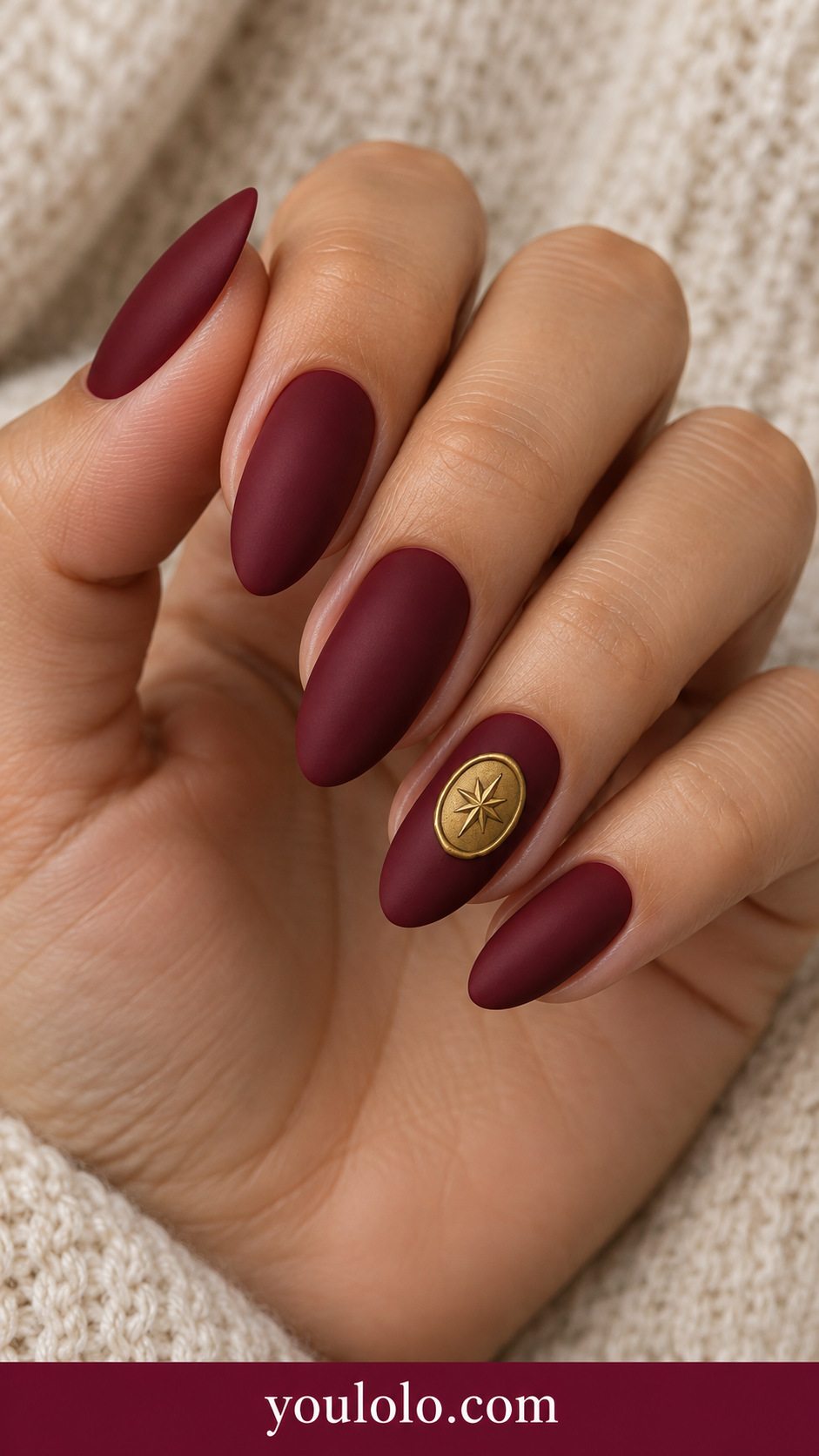 medium almond crimson nails one small flat painted warm gold oval wax seal motif with tiny embossed-look star drawing on ring nail, no actual bulky charm on a naturally relaxed adult hand