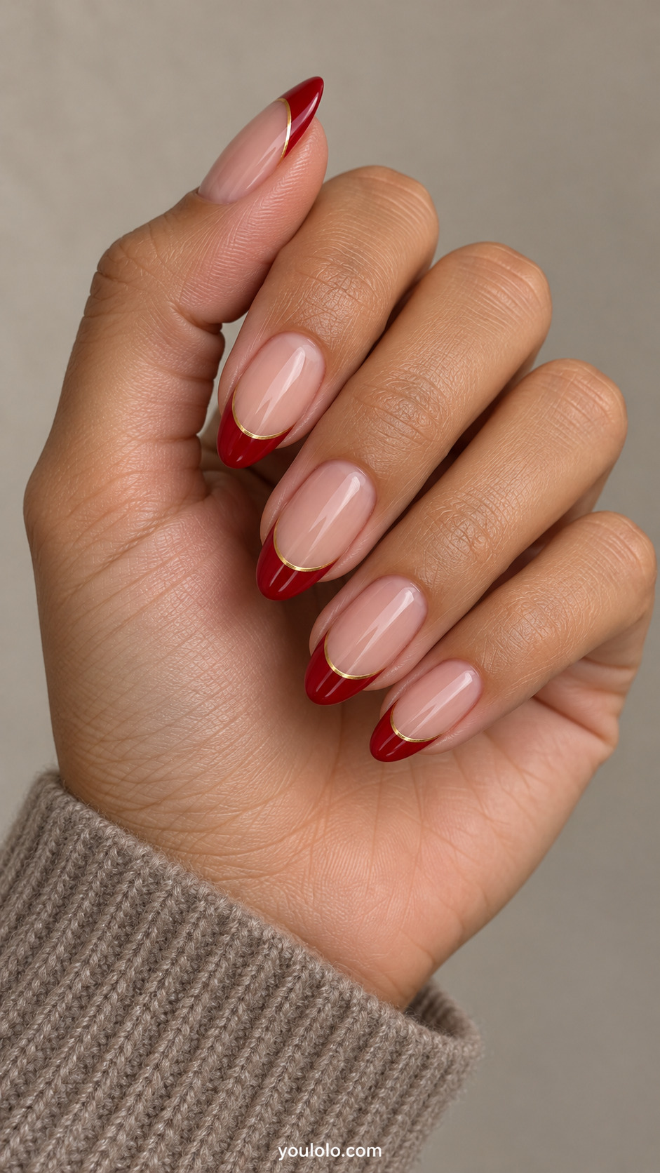 medium almond nude nails, classic cherry-red tips edged at smile by extremely thin metallic gold line on a naturally gathered hand