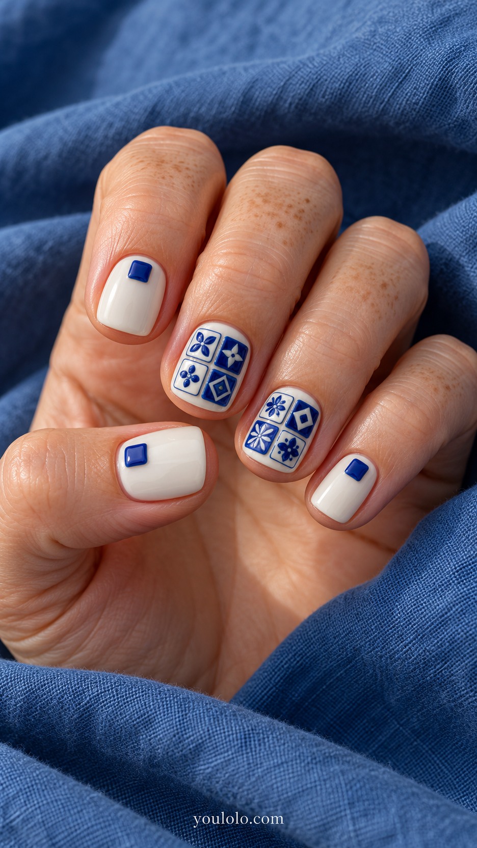 Tiny Ceramic-Tile Relief — Short square nails, creamy white base, two accent nails have four small raised cobalt-blue and white ceramic tile squares with crisp rounded edges and simple hand-painted geometric centers