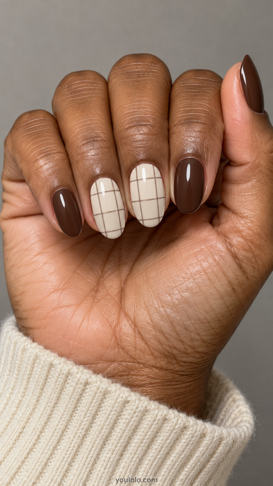 Medium oval nails: cocoa nails with two cream accent nails carrying fine widely spaced taupe windowpane grid, flat paint no sweater texture.