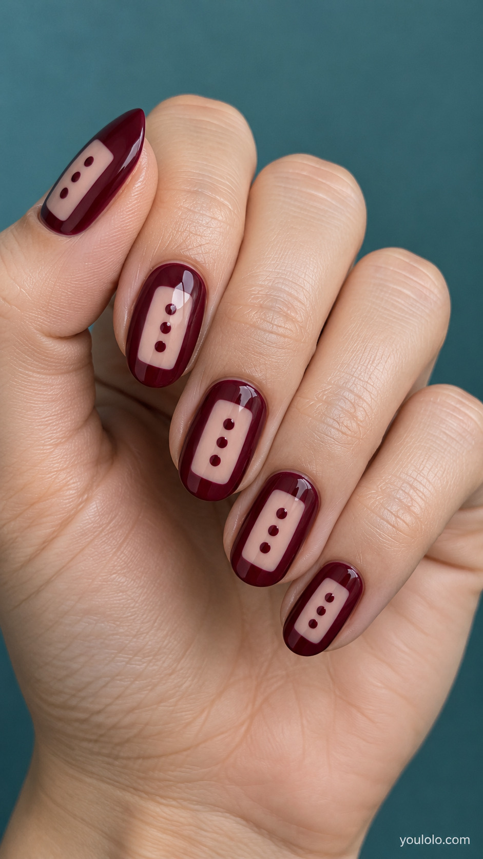 Medium oval nails burgundy with rectangular central nude window on each nail containing three vertical burgundy dots, crisp rounded window corners.