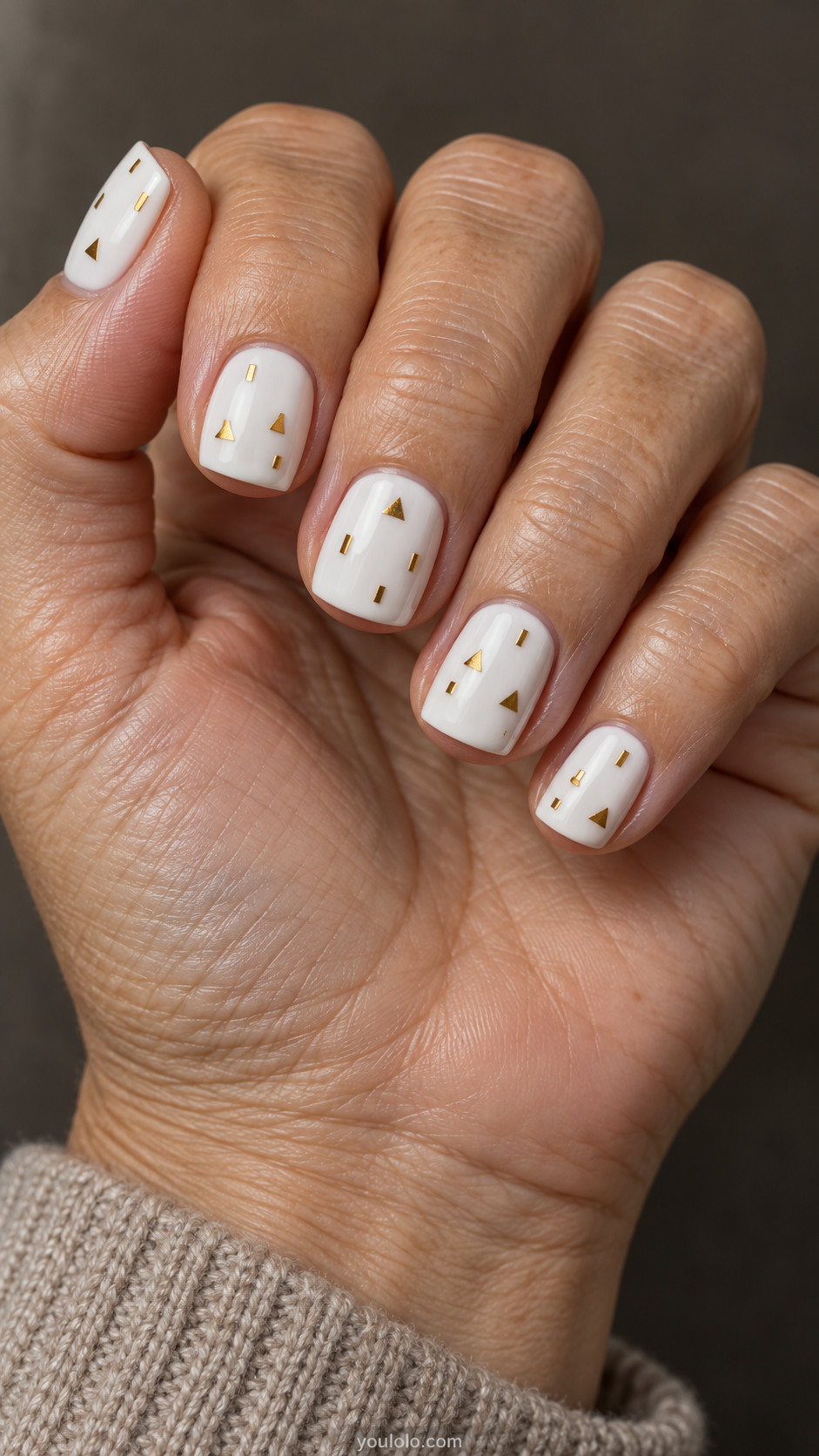 Short square white nails with sparse small gold triangles and rectangles, leaving generous white space