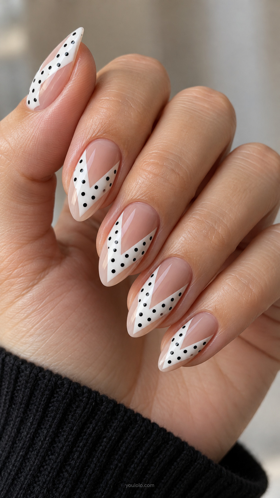 Medium almond nude nails with broad opaque white V chevron inset centered, inside white shape black small polka dots, nude exposed around all edges