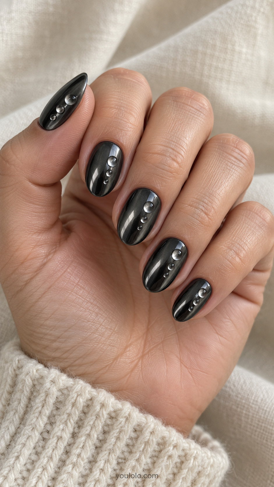 Short almond dark gunmetal chrome nails each with three tiny clear low-profile domed gel droplets, asymmetric spacing, clear not metal studs