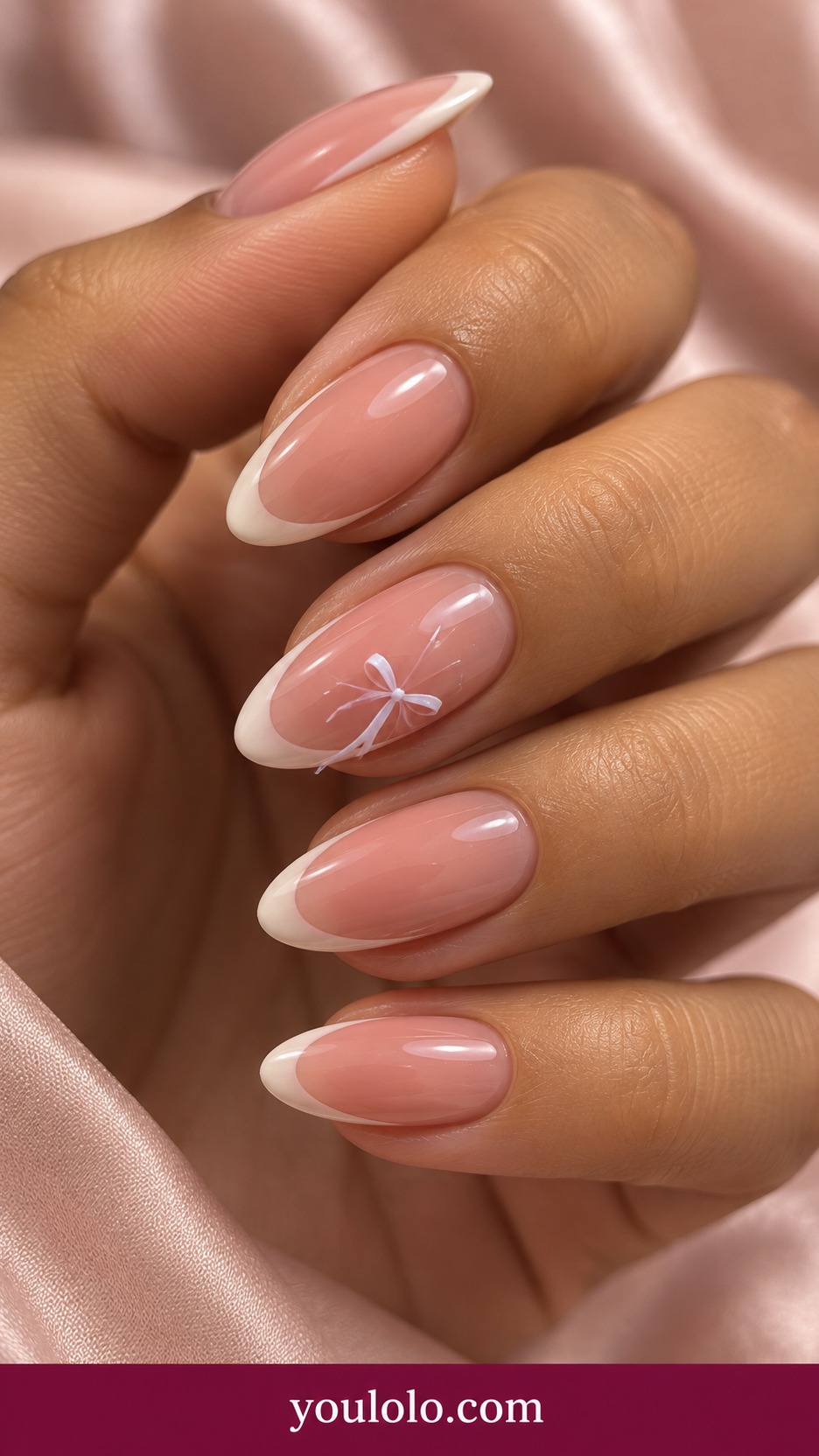 Medium almond sheer pink nails with narrow ivory French and one miniature flat hand painted white bow on an accent on a naturally curled young adult hand
