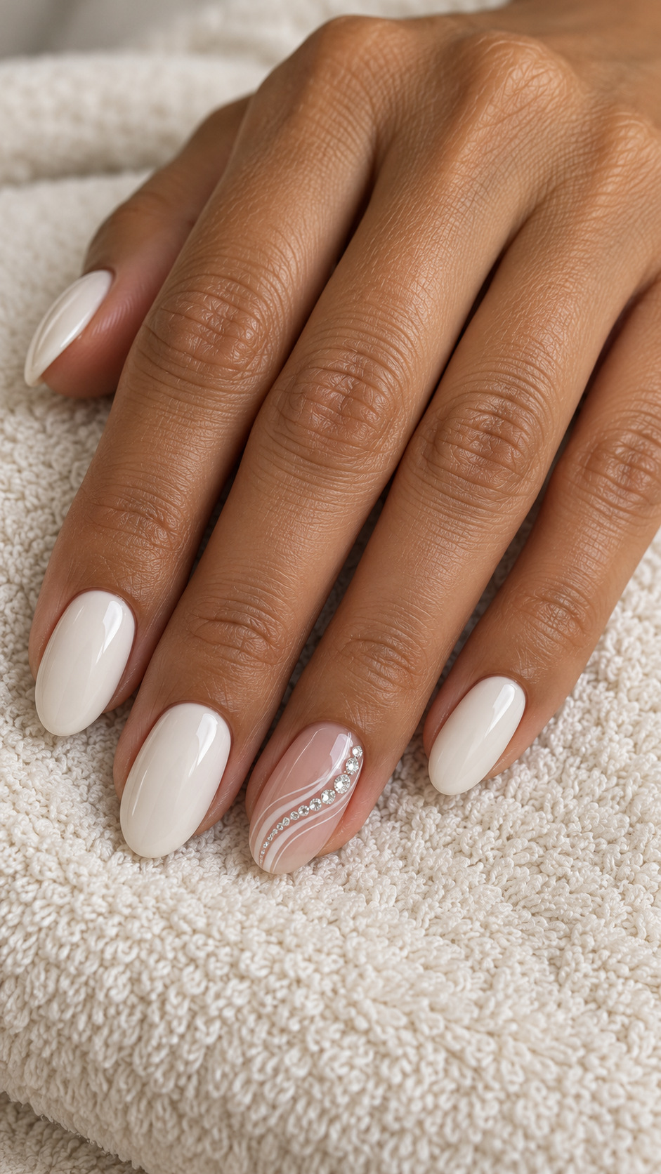 White Swirls with Crystal Highlights: Ivory nails with white swirls and clear crystals on a nude ring finger on a naturally posed adult hand
