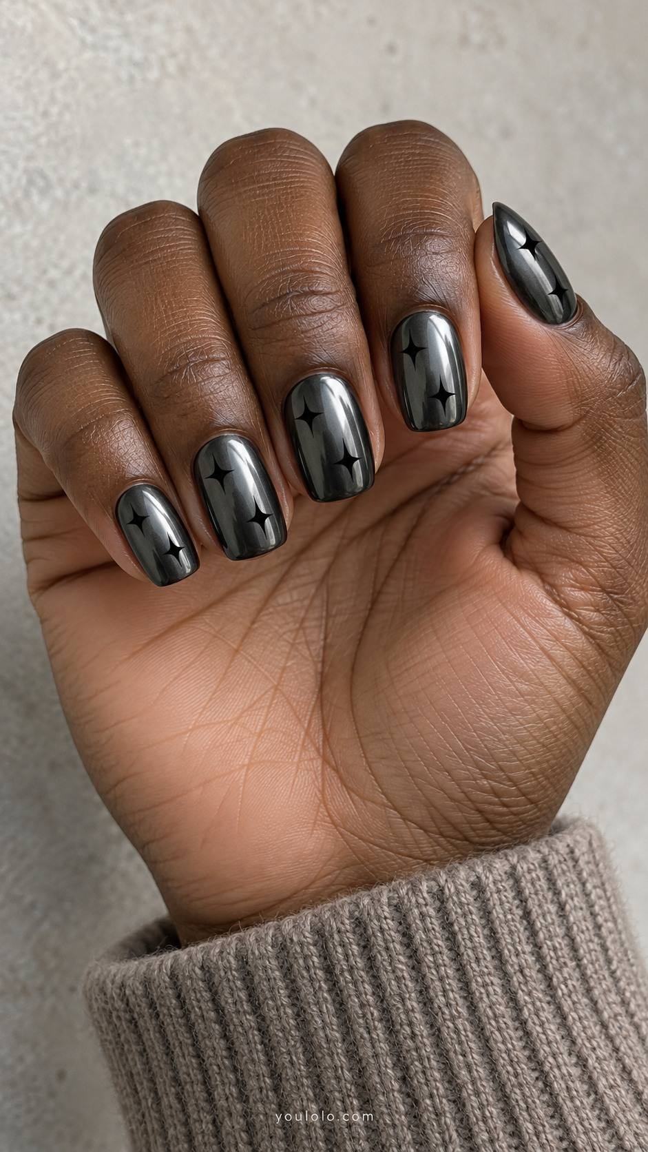 Medium squoval dark gunmetal chrome nails, two small flat matte-black four-point starbursts per nail, irregular placements, no silver decoration
