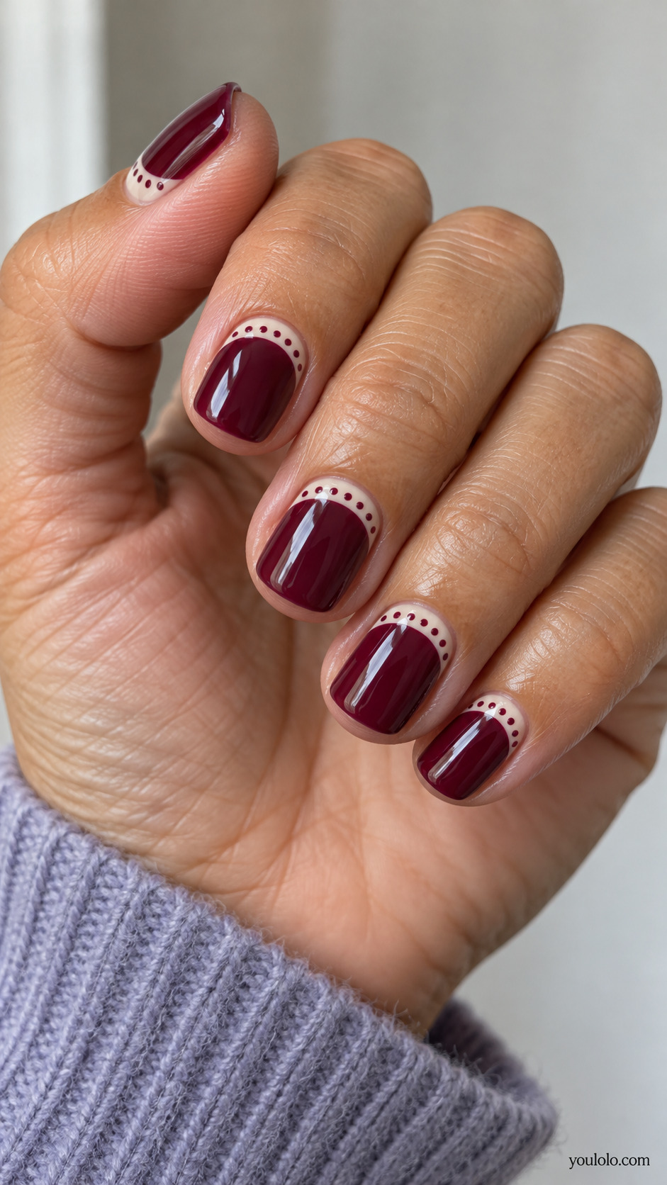 Short squoval burgundy nails, narrow cream horizontal band following curved cuticle with tiny burgundy dots, mostly plain burgundy.