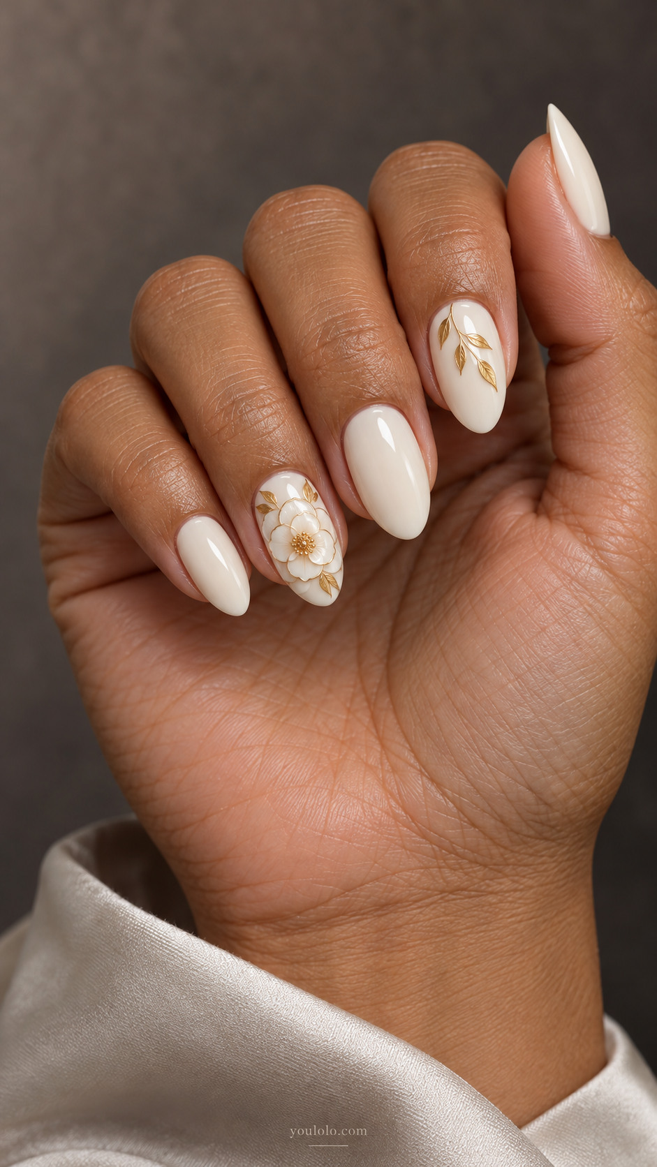 Medium almond ivory nails with a gold-outlined white camellia on the ring nail and gold leaves on the index
