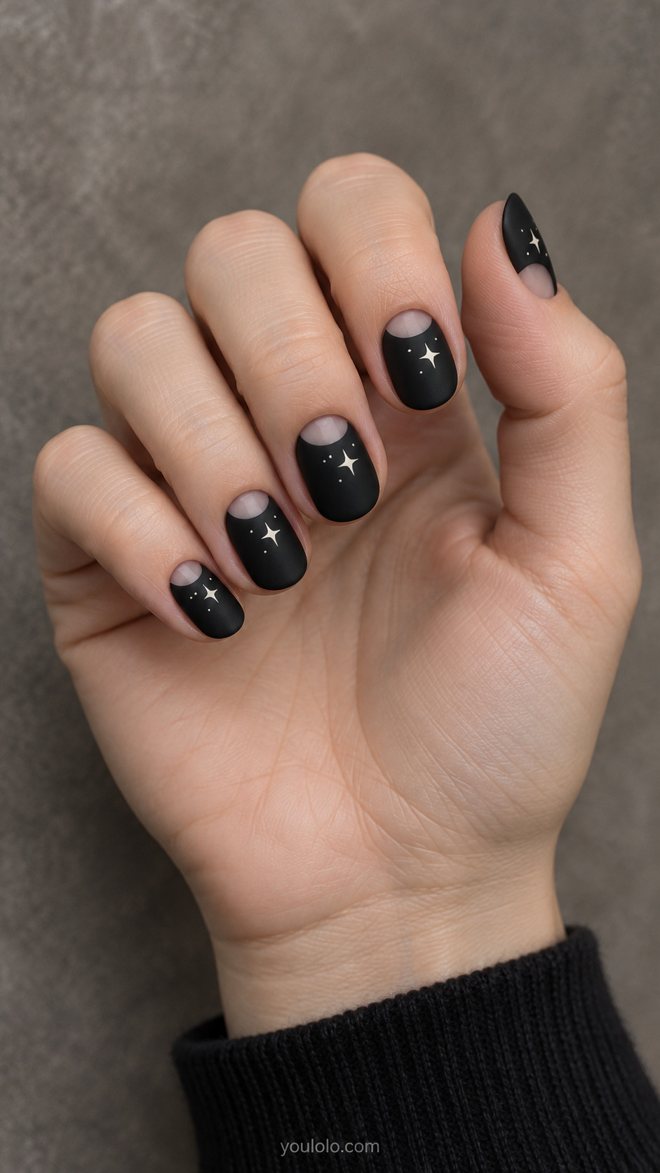 Short matte black oval nails with translucent half-moon cuticle openings and ivory star accents