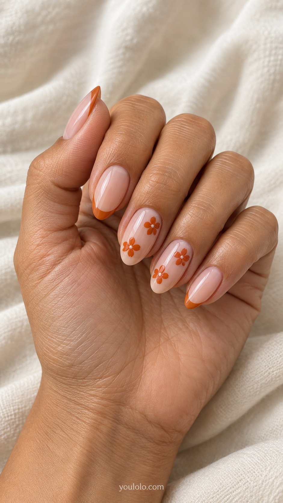Medium almond nails sheer blush with small burnt orange five petal flowers on ring and middle other nails orange thin French tips