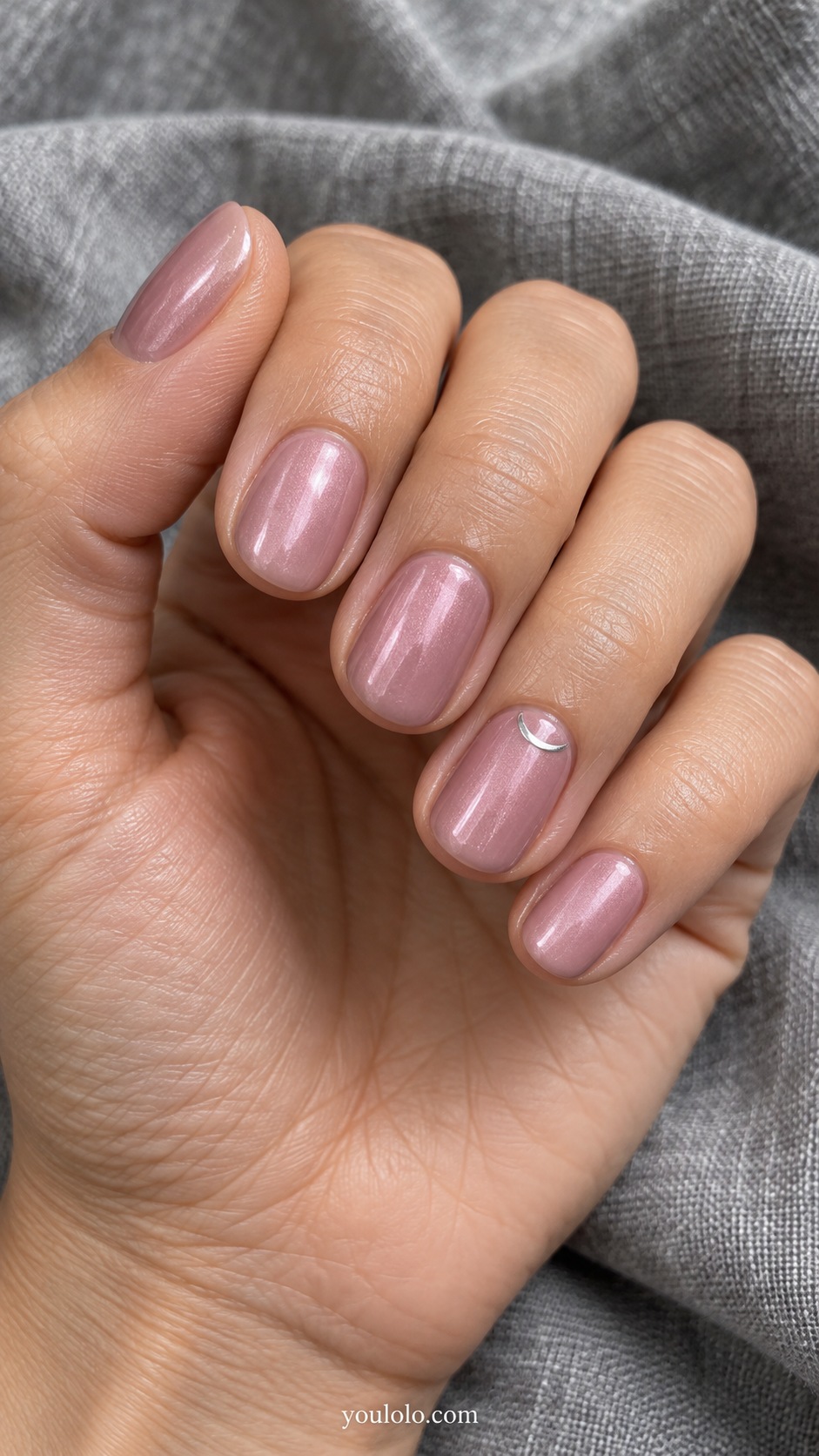 Short oval nails dusty mauve pink base with fine soft pearl sheen, one tiny painted silver crescent on ring nail near cuticle