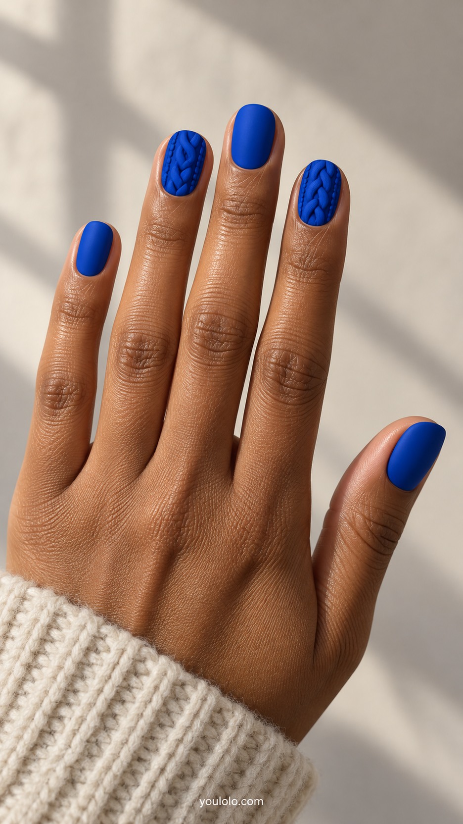Cobalt Cable-Knit Nails — Short rounded nails, matte cobalt blue, index and ring nails have dimensional knitted cable braids in same cobalt and small raised knit stitches, remaining nails smooth matte cobalt, clean sculpted low relief