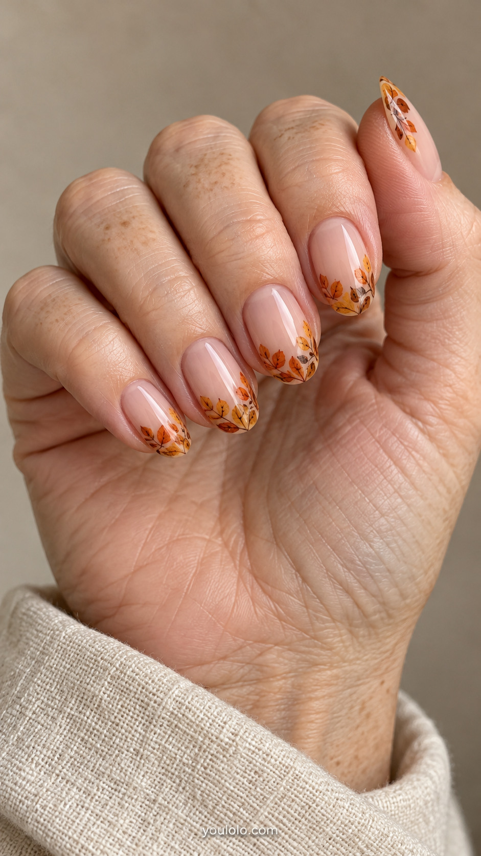 Medium oval nails with transparent blush nails, irregular narrow border of overlapping handpainted amber orange and brown small leaves along free edges only, all cuticle areas empty.