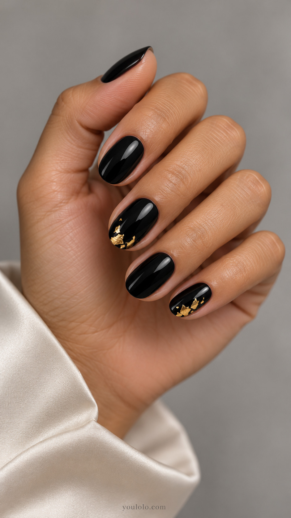 Short black nails with small gold foil clusters near the tips