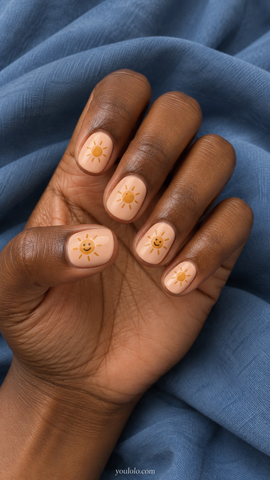 Short round nails peach cream tiny ochre suns on all nails with simple fine brown smiling faces on ring and thumb only