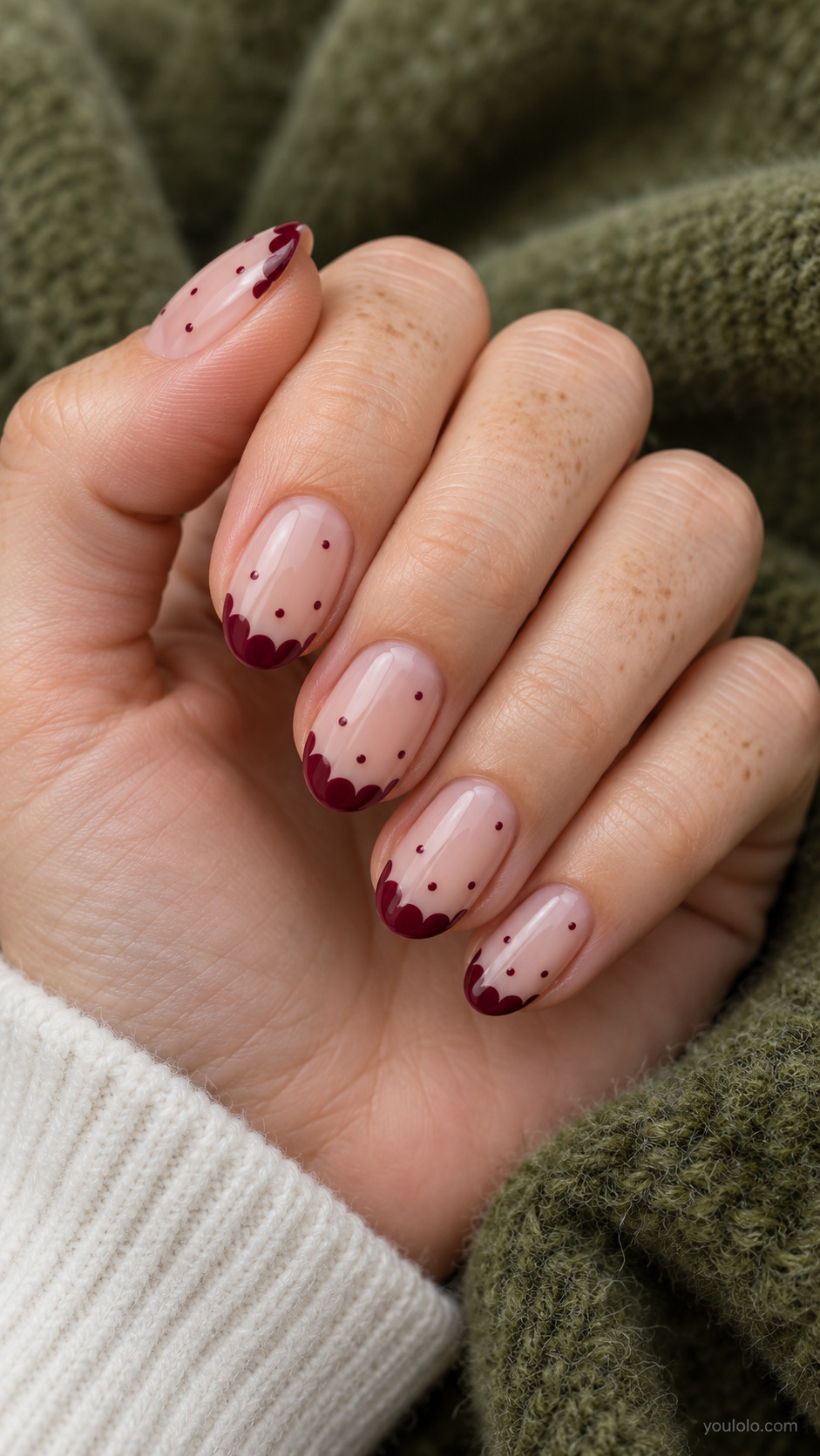 Medium oval nude nails, burgundy semicircle dots overlap just free edge making a soft scalloped tip, isolated tiny burgundy dots farther down nail bed.