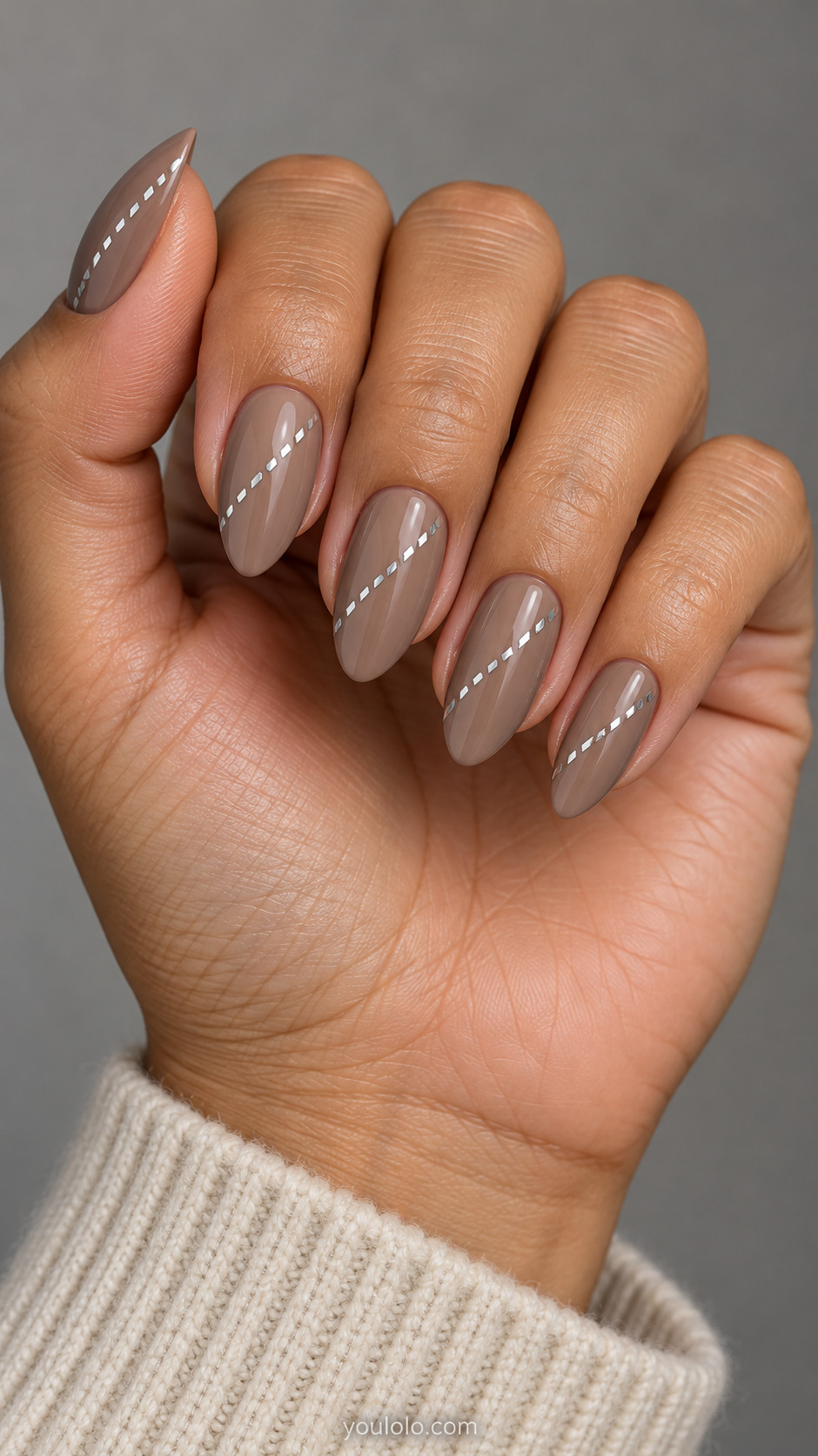 Medium almond nails: warm taupe nails with a single diagonal row of tiny flat silver dashes on each nail, sparse minimal no knit.