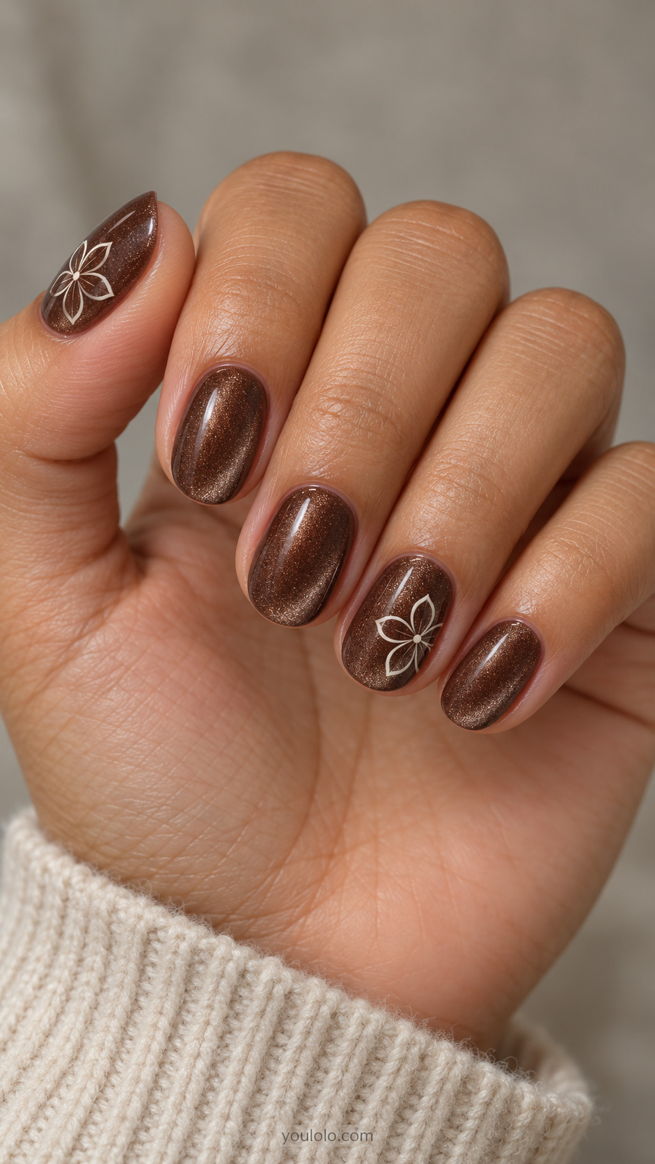 Short oval nails: cocoa brown magnetic velvet all nails; ring and thumb have one fine flat ivory outline five-petal flower with tiny dotted center, no gems.