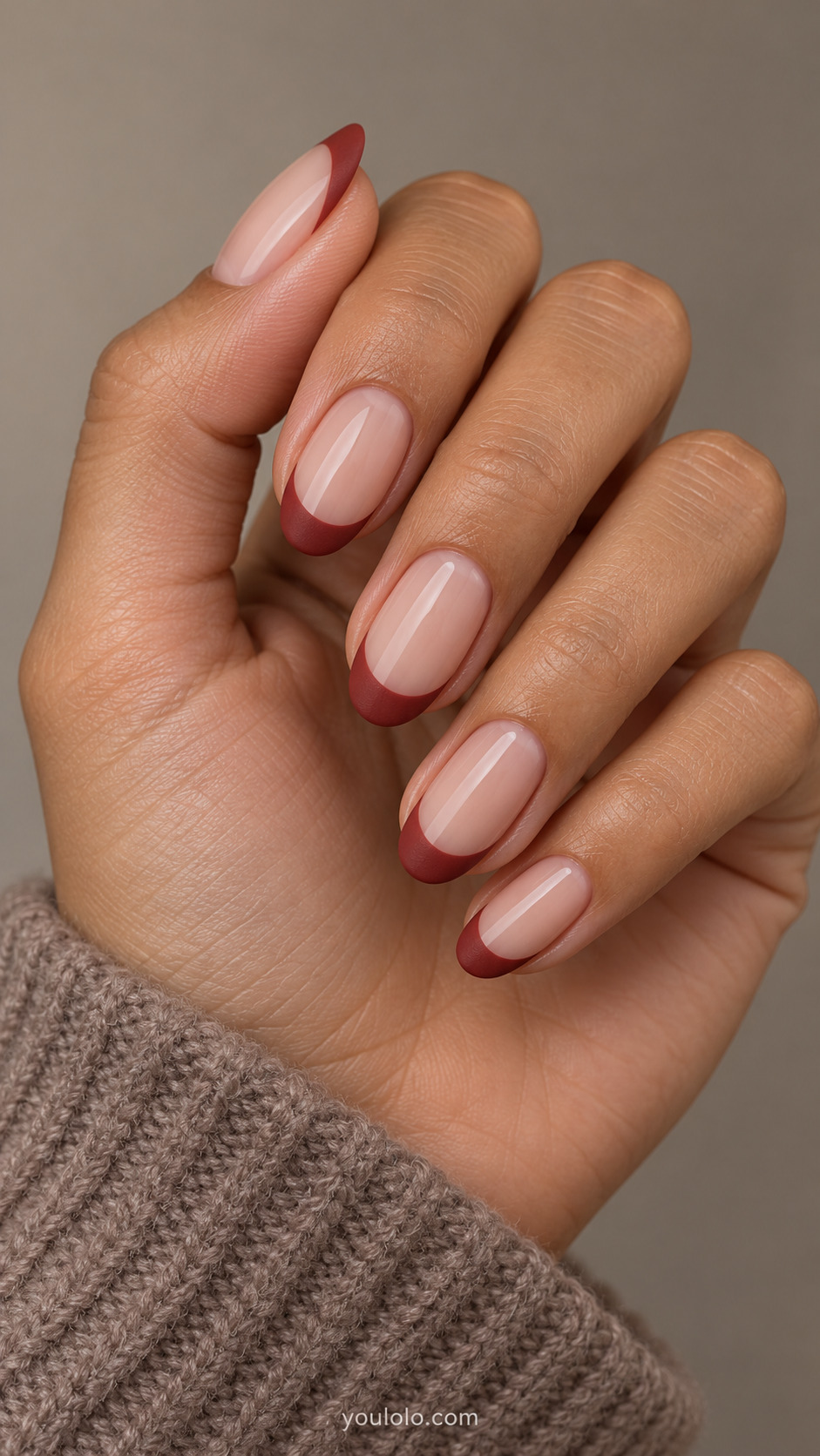 medium oval glossy nude nails, matte brick-red French tips, visible restrained texture contrast on a naturally gathered hand