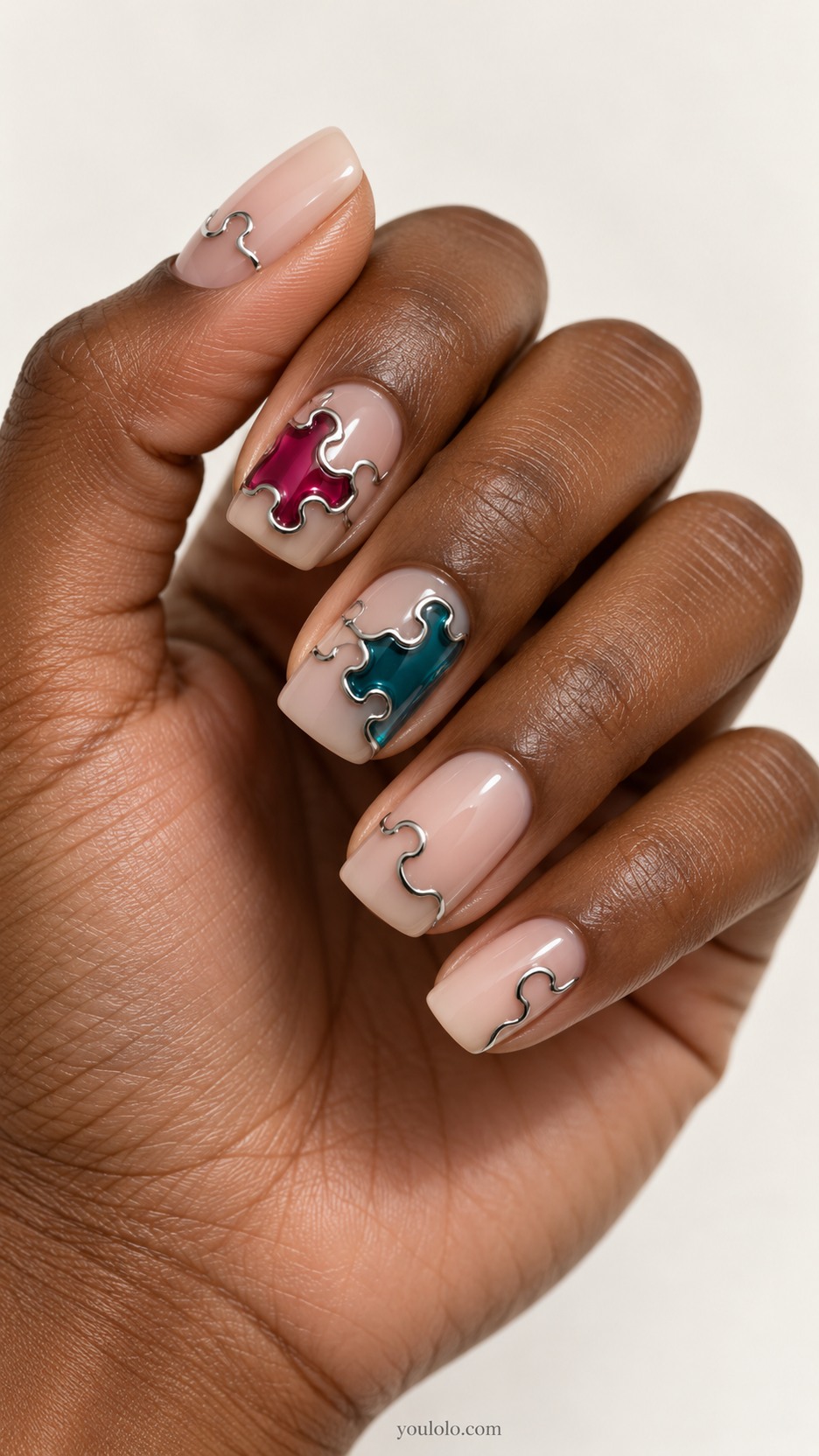 Chrome Puzzle-Piece Nails — Medium square nails, milky nude base, raised polished silver interlocking jigsaw puzzle outlines enclosing translucent raspberry and teal inlays on two accent nails, other nails minimal silver single puzzle-tab curve, all smooth low rounded relief