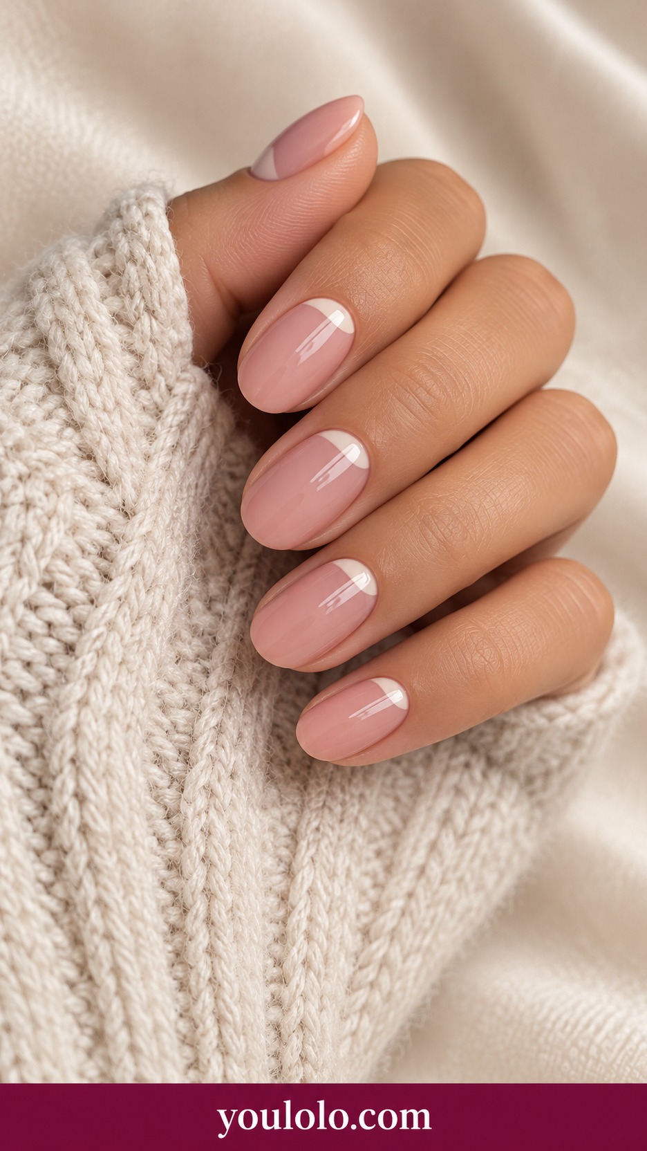 Short round rosy nude nails with a tiny pale ivory half moon at each base glossy on a naturally curled young adult hand