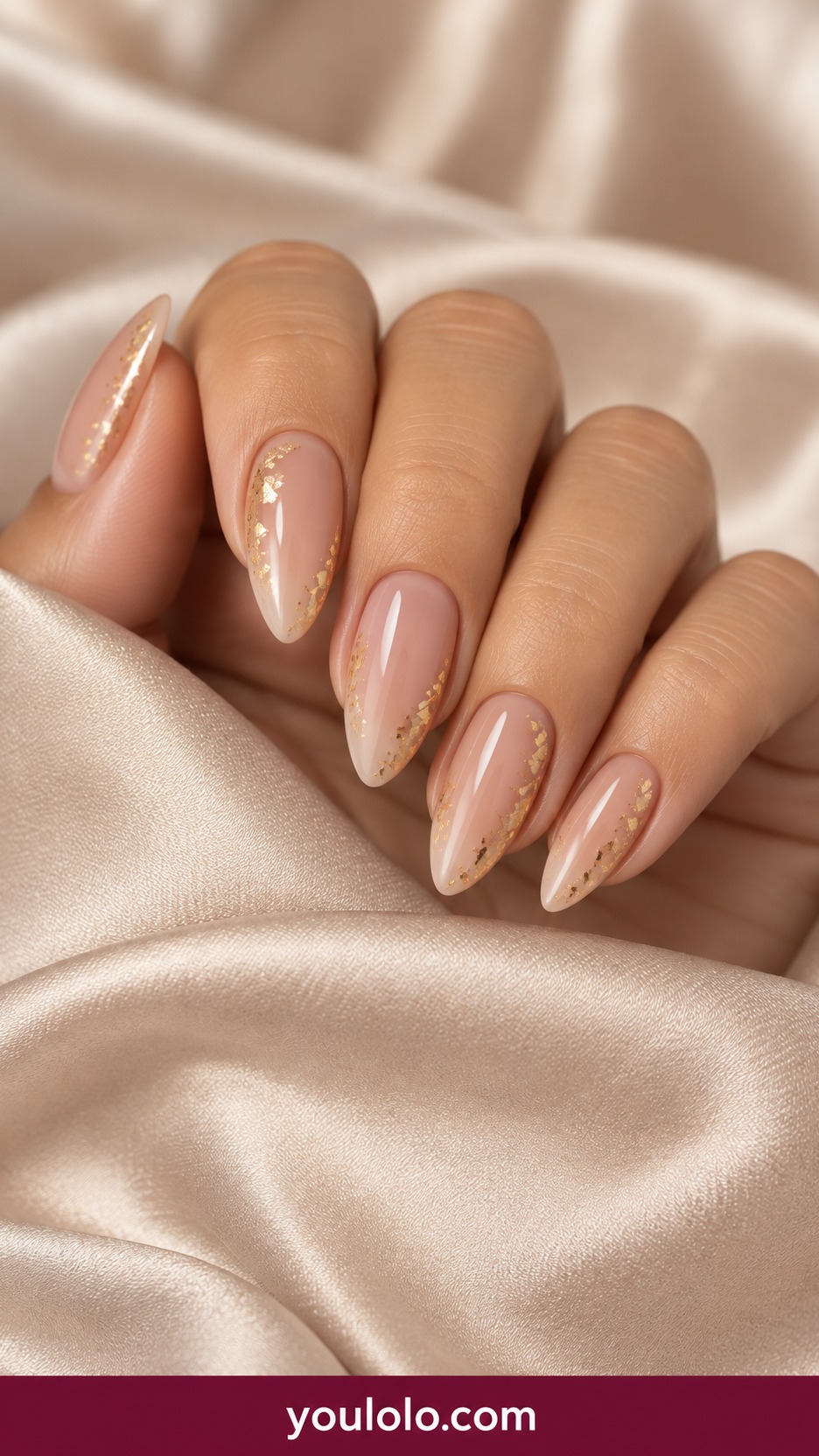 Medium almond sheer warm nude nails with sparse tiny gold foil fragments along lateral edges, center clear on a naturally curled young adult hand