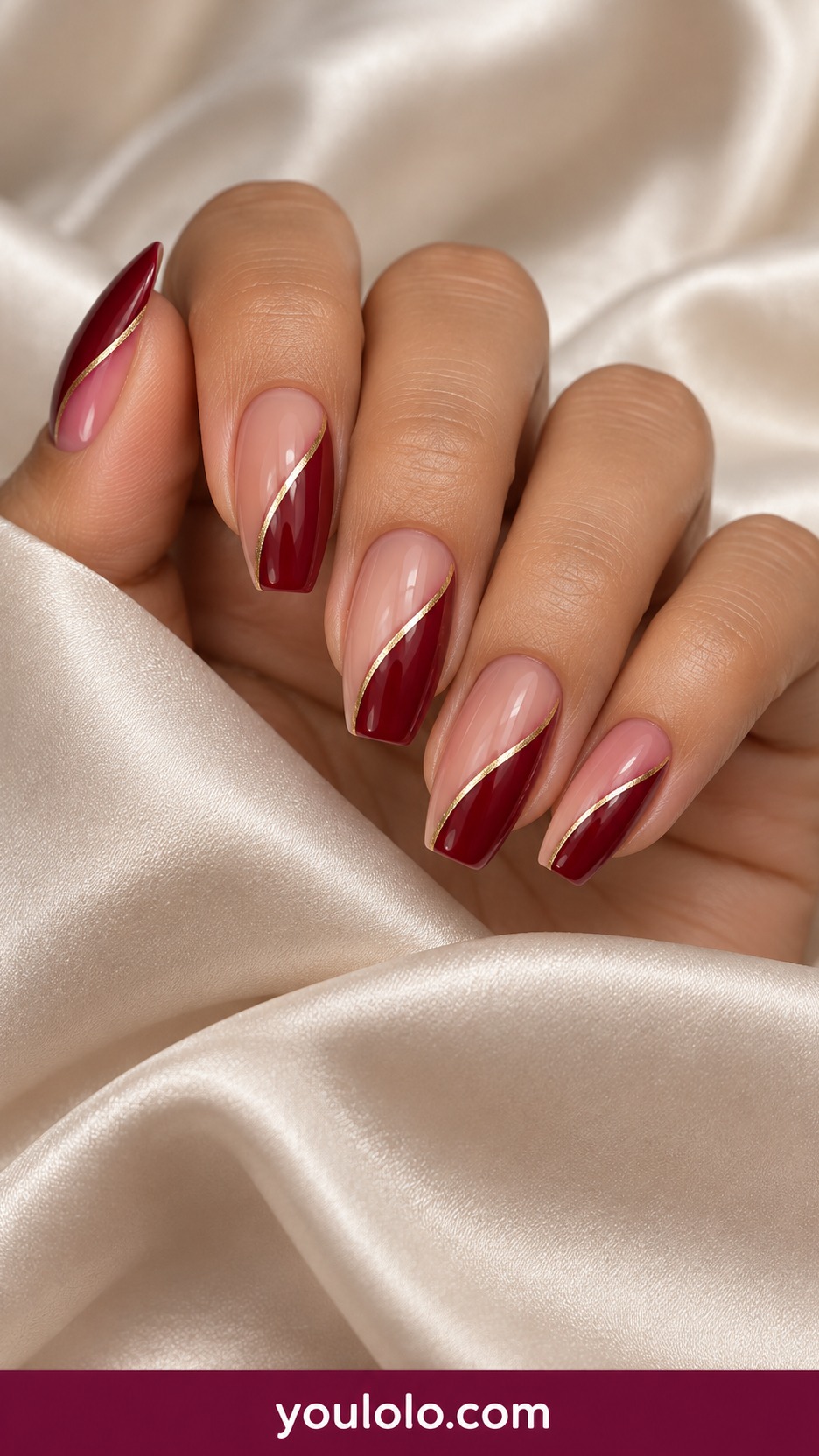 Medium almond nails warm nude with deep red curved diagonal panels and one fine gold separator on a naturally curled young adult hand
